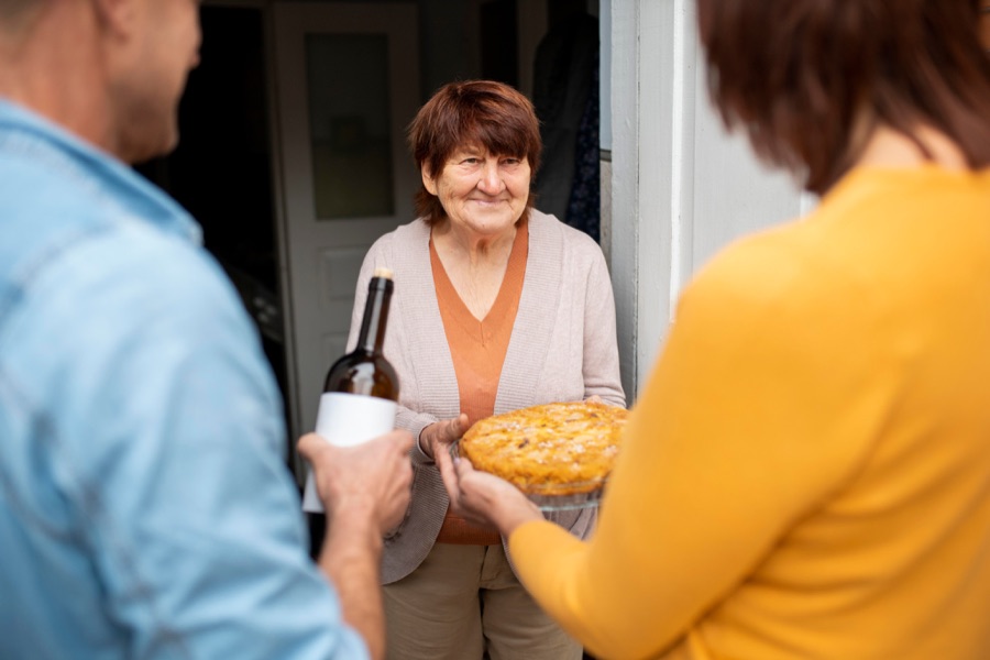 A neighbor handing a freshly baked pie to a senior at the front door