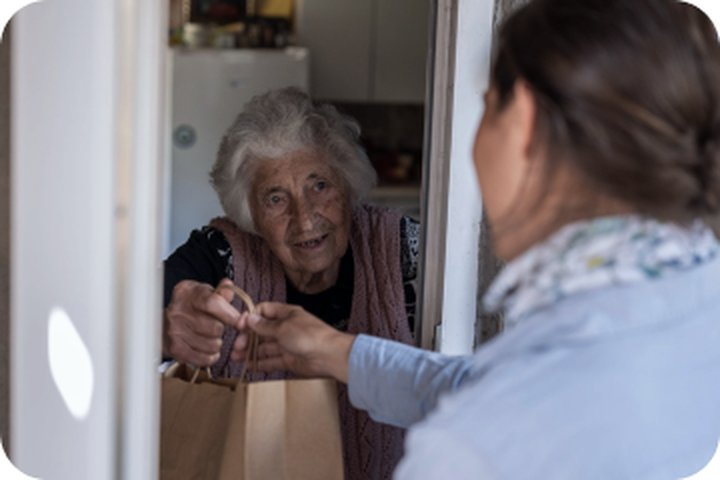 A caregiver hands a bag of meals to a senior at her doorway.