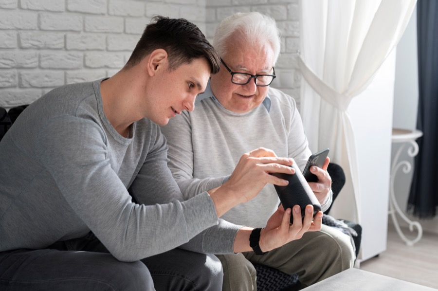 A younger man helping a senior man with a tablet device
